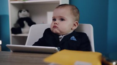 Resmi giysiler içinde konsantre olmuş bir çocuk, bir masada oturuyor, tabletle derinden meşgul.