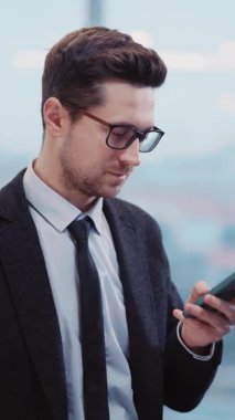 Takım elbiseli bir işadamı telefonunu kontrol eder, hızlı iş dünyasını ve modern iletişimin önemini yansıtır.