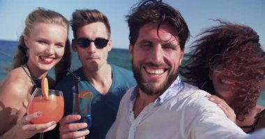 Güneş gözlüklü gülümseyen arkadaşlar selfie çekiyorlar gülüyorlar. Plaj partisinde mutlu hissediyorlar. Yaz adamı teknoloji grubu.