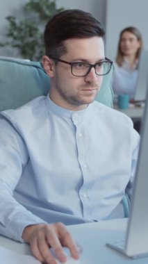 Ofiste bilgisayarda çalışan yakışıklı genç adam. Arka planda iş adamları çalışır. Yavaş çekim