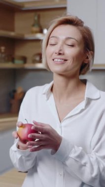 Çekici genç bir kadın mutfakta elma yer. Gülümseyerek mutlu ol. Meyve. Sağlıklı yiyecekler. Yavaş çekim