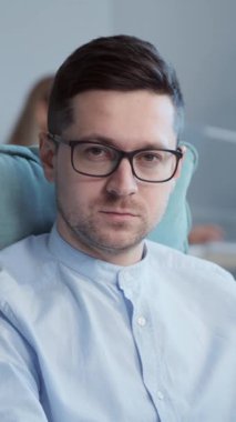 Modern ofiste masa başında oturan kendine güvenen genç ofis müdürünün yakın plan portresi. Siyah gözlüklü, şık mavi gömlekli, doğrudan kameraya bakan yakışıklı bir adam. İçeride. Gündüz