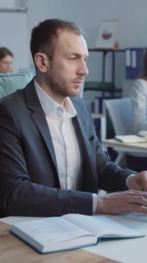 Kafkas 'lı genç işadamının masa başında bilgisayar başında oturup modern ofisteki bilgisayar klavyesinde daktilo kullandığı görüntüler. Başarılı neşeli CEO kameraya bakıp gülümsüyor. Meslektaşlarıyla bulanık bir arkaplan.