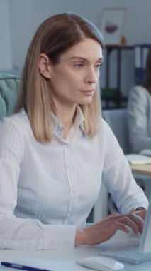 Modern ofisteki güzel tasarımcı koltuğunda oturan kadın çalışan. İş arkadaşlarıyla geçmişi bulanık. Bilgisayarda yazı yazan, kameraya bakıp gülümseyen genç bir kadın görüntüsü. Kapalı.