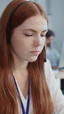 Kulaklıklı, bilgisayar klavyesinde yazı yazan kızıl saçlı genç bir kadının yakın çekim görüntüleri. Gümüş dizüstü bilgisayar kullanan kadın müşteri destek operatörü. Profesyonel operatör konsepti. Resmi kıyafetler, iş günü. Kapalı.