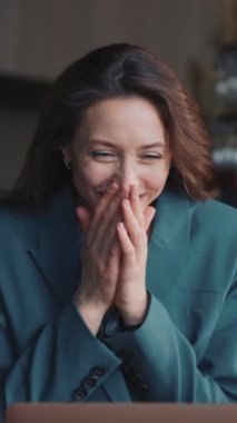 Lokantada çalışan neşeli genç bir kadın. Masada oturan kız, dizüstü bilgisayara bakıyor. Arka planda modern iç mekan. İyi haber, başarılı proje konsepti. Masada bir kadeh beyaz şarap.