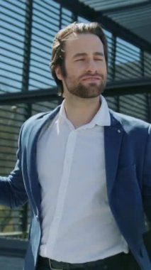 Gülümseyen mutlu sakallı adam iş merkezinin yakınında yürürken aktif olarak dans ediyor. Takım elbise giy. Etrafta insanlar var. İş adamı. Güneş ışığı. Yavaş çekim