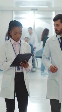 Çok ırklı çift, beyaz sakallı terapisti olan Afro-Amerikan doktor koridorda yürüyor ve konuşuyor. İş arkadaşları. İşbirliği. Tıbbi personel. Hastane.