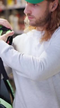 Büyük bir teslimat çantası takan, süpermarkette perakende satış yapan ve kameraya neşeli bakan yakışıklı bir kuryenin portresi. İnsan işgali. Duygular.