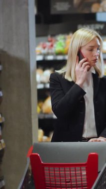 Klasik takım elbiseli resmi iş kadını süpermarketten alışveriş yaparken akıllı telefondan arkadaşını arıyor. Yiyecek alışverişi. Sohbet. Market..