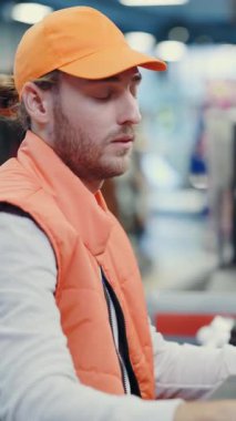 Uykulu, yorgun, sakallı erkek kasiyer beceriksiz işçi müşteriyle ilgisiz konuşuyor kaba tarama aletleri çok hızlı. Kötü hizmetler. Süpermarket.