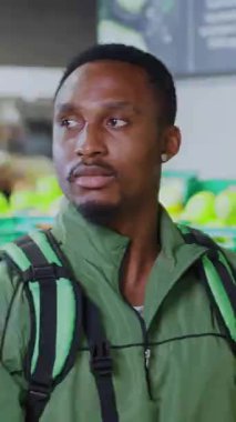 Marketin içinde kameraya çapraz kollar pozu veren yeşil çantalı kendinden emin genç kuryenin portresi. Süpermarket çalışanları. Yemek teslimatı.