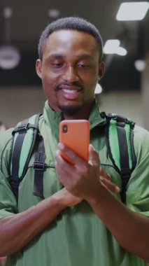 Akıllı telefon mesajları taşıyan neşeli siyahi genç kurye süpermarkette eğlence uygulaması kullanarak müşteriye kur yapıyor..