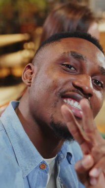 Yüz portresi yakışıklı Afrikalı genç adam arkadaşlarıyla kahve dükkanında takılıyor ve komik bir selfie videosu kaydediyor. Vlogger yaşam tarzı. Arkadaşlar.