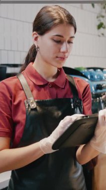 Modern kafeteryadaki kameraya gülümseyen dijital tablet bilgisayar kullanan çekici bir bayan kahve dükkanı çalışanı. Mesleğiniz? Kişi portresi.