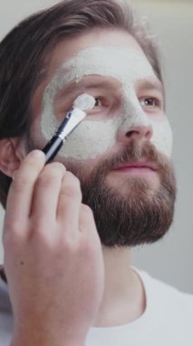 Stüdyo arka planında fırça reklamı ile yüz kilinden maske takan profesyonel erkek modelin yan görüntüsü..