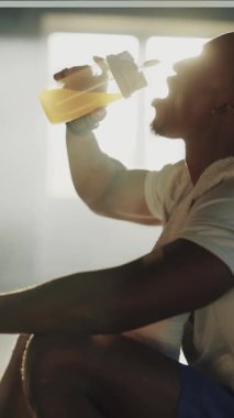 Afrikalı Amerikalılar, spor salonunda egzersiz yaptıktan sonra şişeden protein içeceği içen güçlü vücutgeliştirme sporcusu. Egzersiz konsepti.