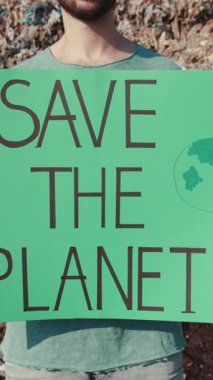 Bir katılımcının elinde gezegeni çevreci bir mitingde kurtarmak için acil eylem çağrısında bulunan parlak yeşil bir işaret var.