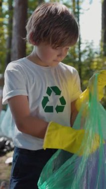 Geri dönüşüm tişörtlü bir çocuk doğayı özenle temizliyor, çevresel sorumluluk ve farkındalığı teşvik ediyor.