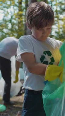 Renkli eldivenleri olan genç bir çocuk dışarıda çöp topluyor, çevre bilincini ve sorumluluğunu arttırıyor.