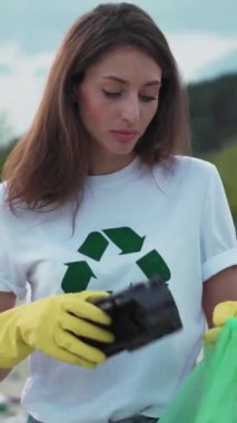 Geri dönüşüm temalı gömlekli bir kadın, yerel çevresini iyileştirmek için bir toplum temizliğine katılıyor