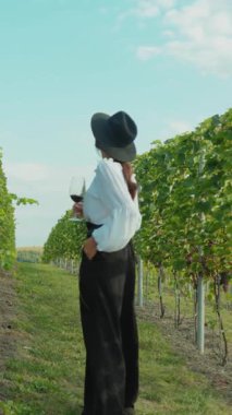 Şık bir birey, güneşli gökyüzünün altında, şatafatlı bir üzüm bağında şaraptan zevk alır.