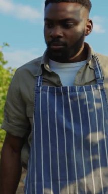 Klasik çizgili önlük giyen çok yetenekli bir erkek aşçı dışarıda duruyor ve mutfak sanatını ve sanatını inceliyor.