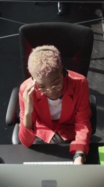 Parlak kırmızı bir takım elbise ve kulaklık giyen odaklanmış bir birey bilgisayardaki işlerine tamamen dalmış durumda.