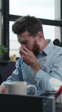 Modern bir ofiste, bir adam görev ve sorumluluklarına özenle odaklanırken yorgunluk belirtileri gösterir.