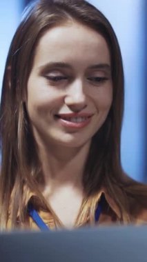 Genç bir kadın, modern bir ofis ortamında dizüstü bilgisayarını kullanırken sevinçle gülümsüyor.