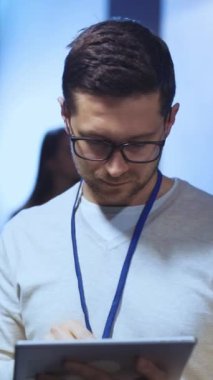 Gündelik süveter giyen ve gözlük takan genç bir adam modern ofis ortamında tablet üzerinde çalışıyor.