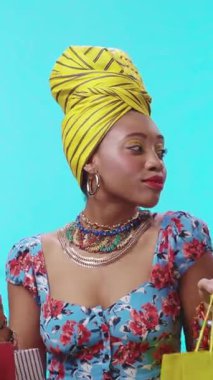 Neşeli bir kadın renkli bir çiçekli elbiseyle parlıyor ve parlak bir arkaplana karşı çarpıcı aksesuarlar takıyor..