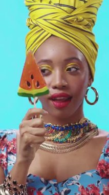 Şık bir kadın büyük bir karpuz lolipopu ile poz veriyor, canlı aksesuarlarını ve şık kıyafetlerini vurguluyor.