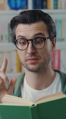 Gözlük takan genç bir adam kütüphanede otururken ilginç bir kitap okumaya dalmış.