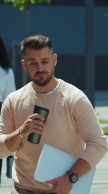 Genç bir profesyonel bugün modern iş hayatı dengesini temsil eden bir dizüstü bilgisayar ve kahveyle güvenle dışarı çıkıyor.