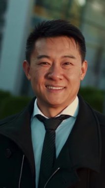 Kendine güvenen bir birey şık bir takım elbise giyerken sıcak bir şekilde gülümsüyor, canlı ve modern bir şehir manzarasına karşı.