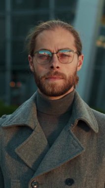 Şehir ortamında, modaya uygun gözlüklü şık bir adam kendine güvenen bir duruş sergiliyor.