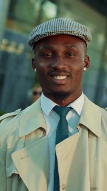 Şık ve modaya uygun genç bir adam modaya uygun bir trençkot ve şık bir şapkayla modern tarzda poz verir.