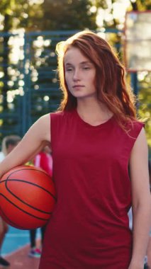 Genç bir kadın, şehir ortamında kararlılığını ve gücünü gösteren bir basketbol topunu kendinden emin bir şekilde tutuyor.