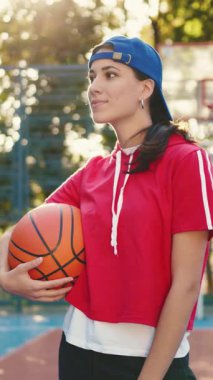 Kendine güvenen genç bir kadın bir basketbol topunu elinde tutuyor ve etkileyici atletizmini şehir sahasında sergiliyor.