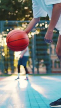 Yetenekli bir oyuncu basketbol sahasında gün batımının sıcacık, altın parıltısında basket topu sürüyor.