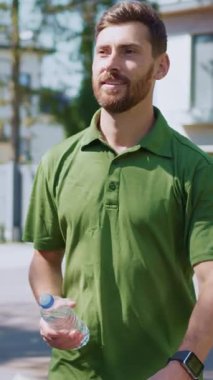 Neşeli bir adam dışarıda keyifli bir yürüyüş yapıyor, su şişesini tutarken pozitif ve sağlıklı.