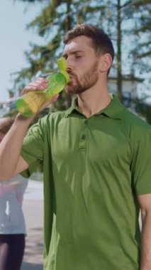 Parlak yeşil tişörtlü bir adam dışarıda egzersiz yaparken ferahlatıcı bir içeceğin keyfini çıkarıyor.