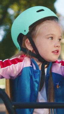 Genç bir kız açık havada bisiklet sürmekten zevk alıyor. Renkli bir kask ve şık bir ceket giyiyor.