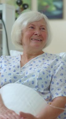 Kabarık beyaz saçlı yaşlı bir kadın hastane yatağında oturuyor. Muazzam bir sıcaklık ve dayanıklılık yayıyor.