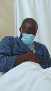 Hasta yatakta dinleniyor, maske takıyor, hastane ortamında, sağlık konularını yansıtıyor..