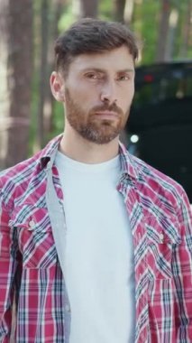 Sakallı bir adam, güzel, doğal ormanlık bir çevreyle çevrili iken düşünceli bir şekilde durur.