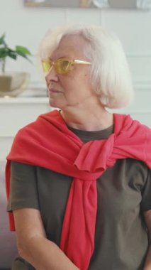 Zarif ve modaya uygun yaşlı bir kadın şık gözlüklerini ve canlı süveterini sergilerken kendine güvenerek poz verir.