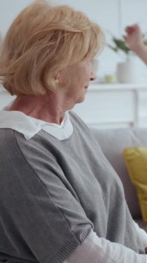 Altın çağındaki son sınıf bir kadın, rahat ve modern bir oturma odasında otururken düşünceli bir şekilde yansıtır.