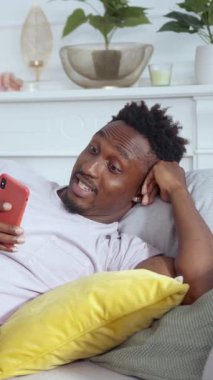 Bir adam şık, modern bir kanepeye uzanır, akıllı telefonuna dalmış, rahat bir yaşam alanı içinde.